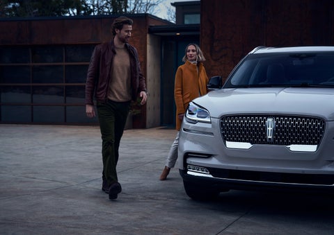 A man and a woman approaching a 2024 Lincoln Aviator® SUV, which illuminates certain lights when they are close | Nick Mayer Lincoln Mayfield in Mayfield Heights OH
