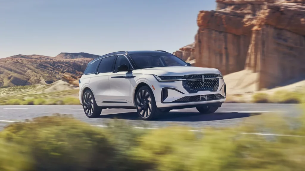 2025 Lincoln Nautilus Black Label in white with a black roof driving through a desert landscape, with rocky cliffs and blue skies in the background.