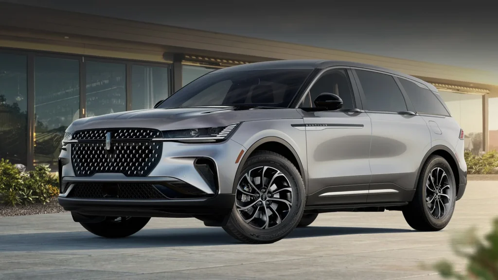 2025 Lincoln Nautilus Premiere in silver parked in front of a modern glass building at sunset, showcasing its sleek design and signature grille.