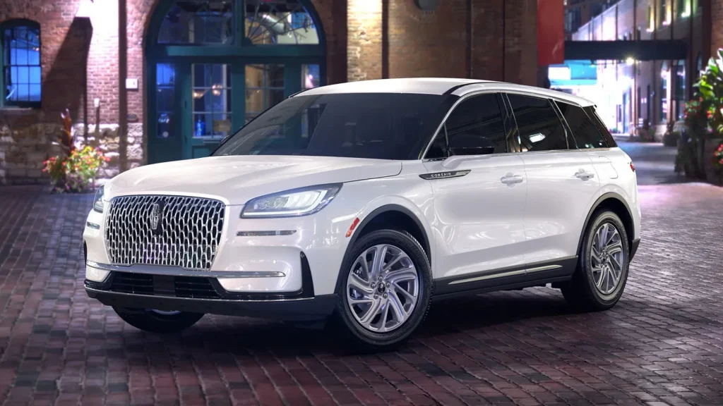 White 2025 Corsair® Premiere luxury SUV parked on brick road under city lights.