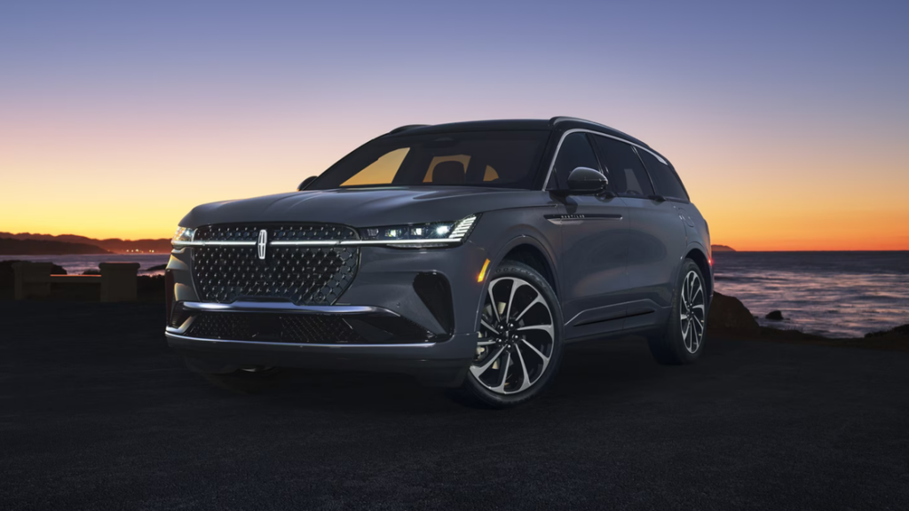 Front-side view of a dark gray 2025 Lincoln Black Label Nautilus parked near the ocean at sunset.