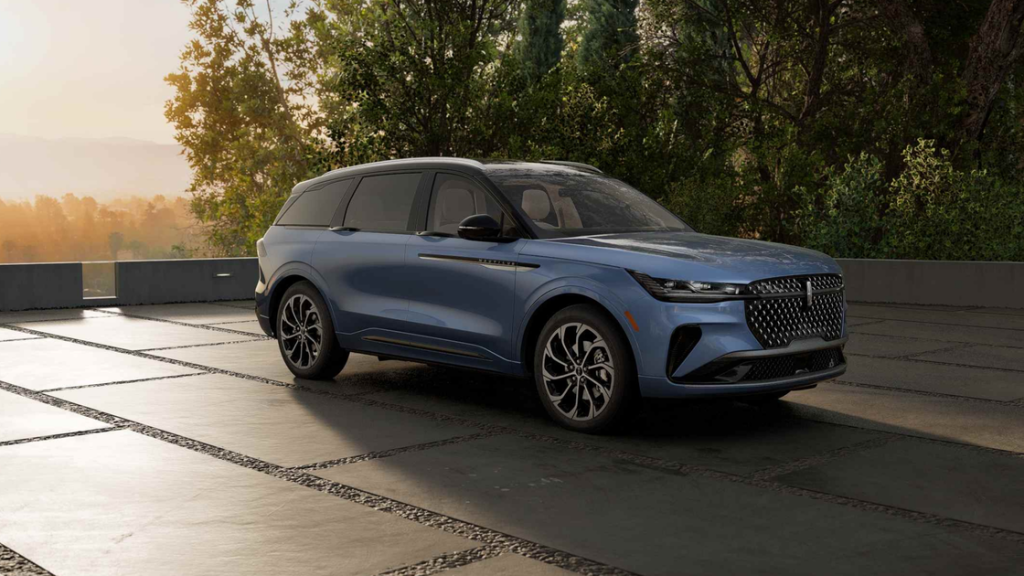 Front-side view of a blue 2025 Lincoln Nautilus parked on a stone patio at sunset with trees in background.