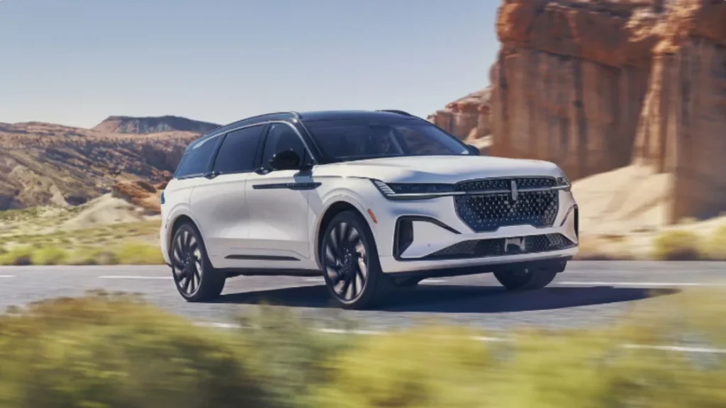 White 2026 Lincoln Nautilus® SUV driving through desert canyons, featuring aerodynamic curves and a bold grille.