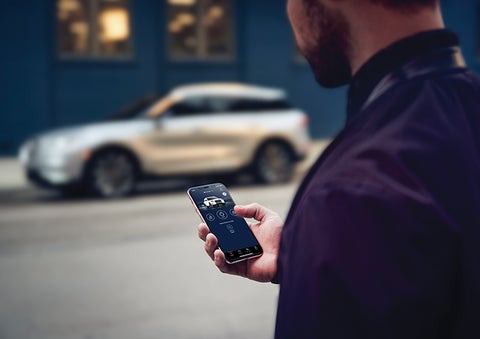 A person is shown interacting with a smartphone to connect to a Lincoln vehicle across the street. | Nick Mayer Lincoln Mayfield in Mayfield Heights OH