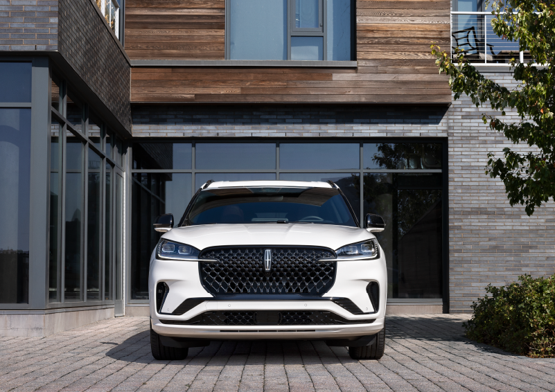 A white 2025 Lincoln Aviator® SUV is shown parked outside a modern building with gray brick and wood accents. | Nick Mayer Lincoln Mayfield in Mayfield Heights OH