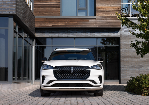 A white 2025 Lincoln Aviator® SUV is shown parked outside a modern building with gray brick and wood accents. | Nick Mayer Lincoln Mayfield in Mayfield Heights OH