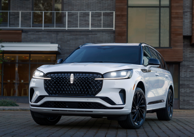 A white 2025 Lincoln Aviator® SUV is shown parked outside a modern building with gray brick and wood accents. | Nick Mayer Lincoln Mayfield in Mayfield Heights OH