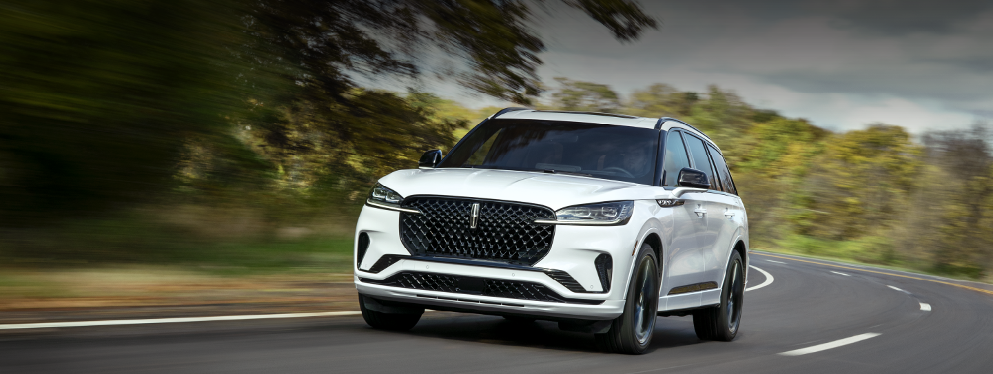 A white 2025 Lincoln Aviator® SUV is being driven down a road lined with trees. | Nick Mayer Lincoln Mayfield in Mayfield Heights OH