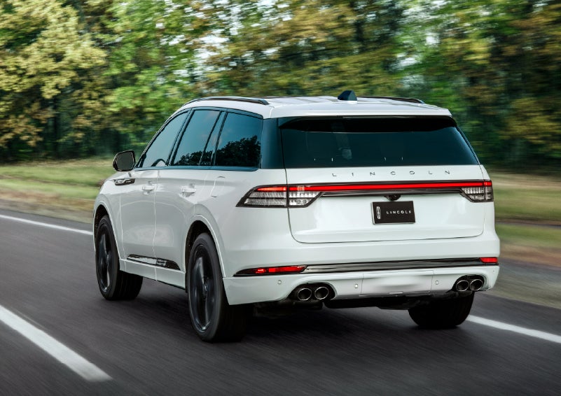 A white 2026 Lincoln Aviator® SUV is being driven away down a road lined with colorful trees. | Nick Mayer Lincoln Mayfield in Mayfield Heights OH