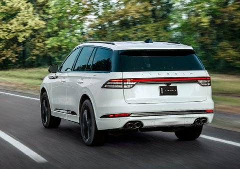 A white 2026 Lincoln Aviator® SUV is being driven away down a road lined with colorful trees. | Nick Mayer Lincoln Mayfield in Mayfield Heights OH