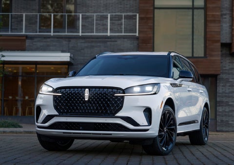 A 2026 Lincoln Aviator® Reserve model is shown with the available Jet Appearance Package parked near a restaurant. | Nick Mayer Lincoln Mayfield in Mayfield Heights OH