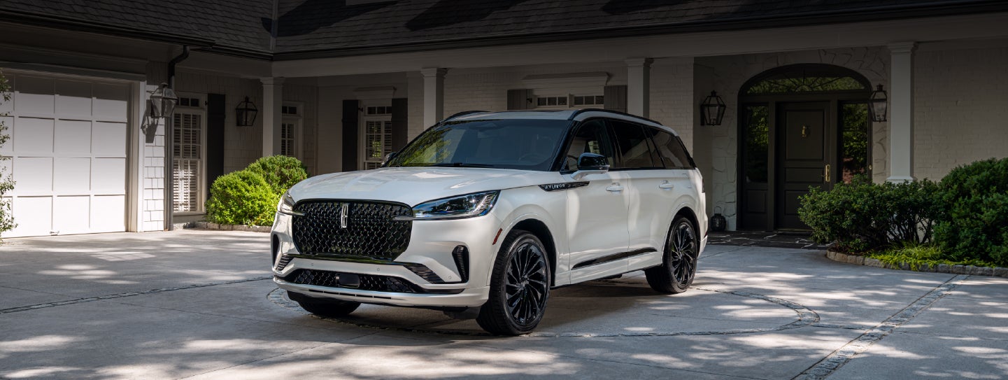 A white 2026 Lincoln Aviator® SUV is parked in the driveway of a luxury home. | Nick Mayer Lincoln Mayfield in Mayfield Heights OH