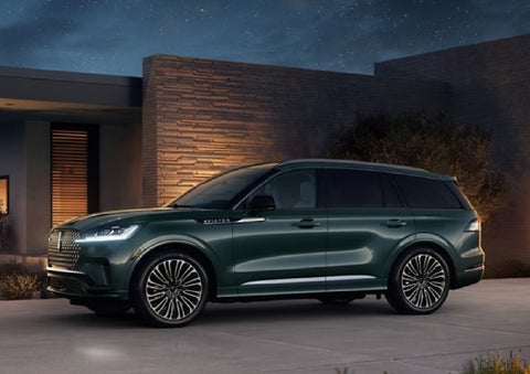 A green 2027 Lincoln Aviator® SUV is parked outside a contemporary home. | Nick Mayer Lincoln Mayfield in Mayfield Heights OH