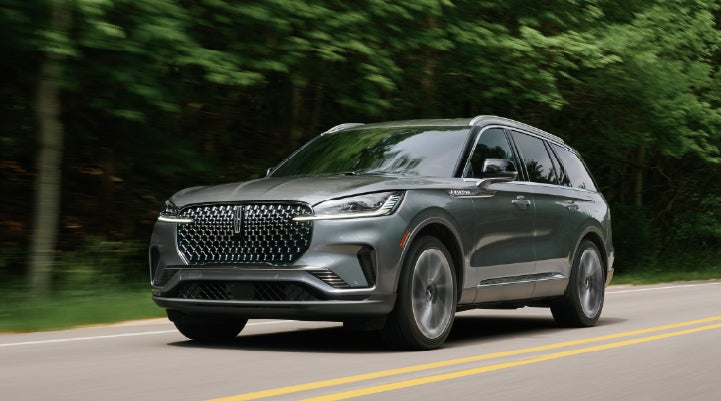 A 2027 Lincoln Aviator® SUV is being driven down a road lined with trees. | Nick Mayer Lincoln Mayfield in Mayfield Heights OH
