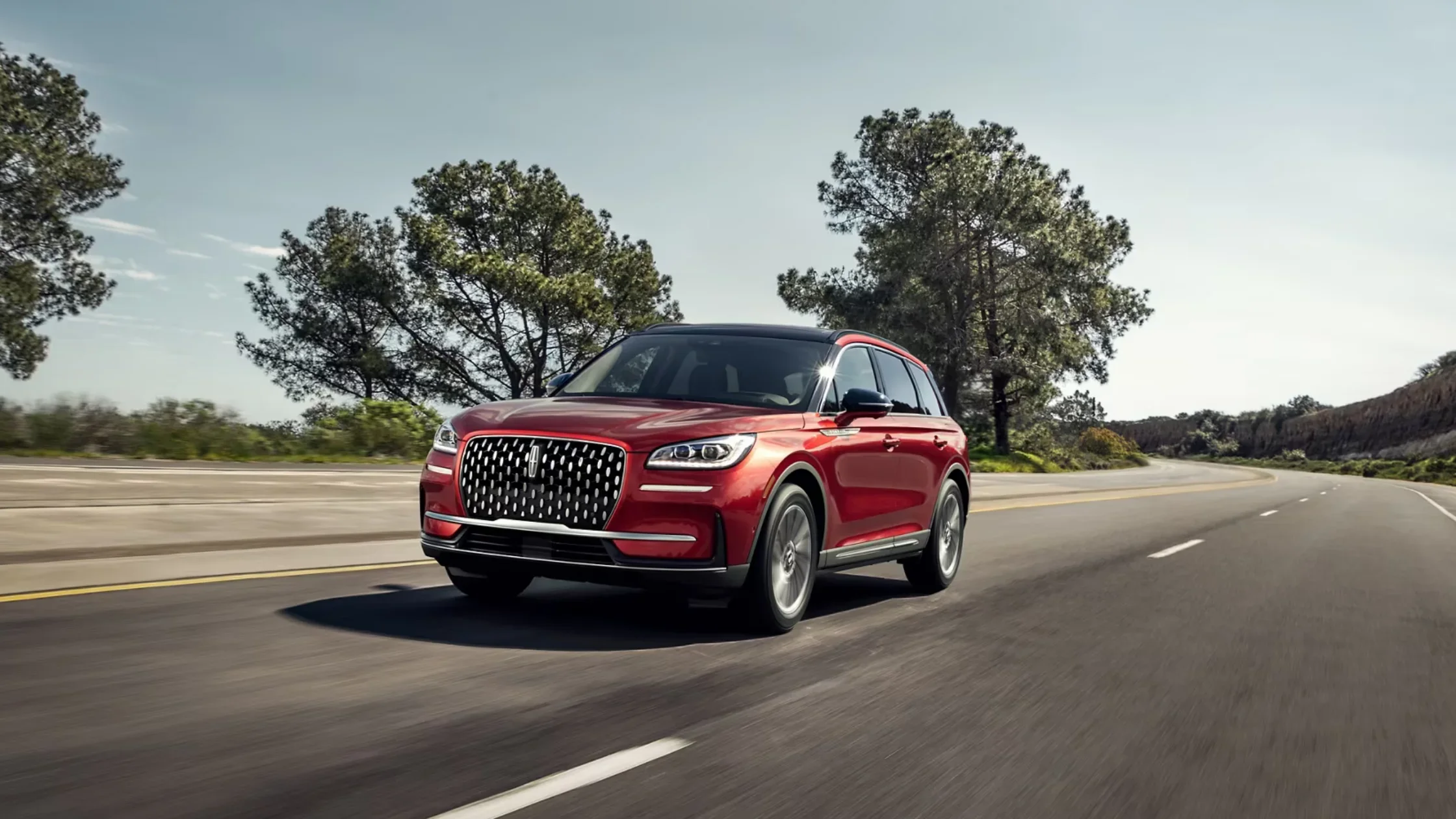 Red 2025 Lincoln Corsair Reserve SUV driving on highway with chrome grille and LED headlights.