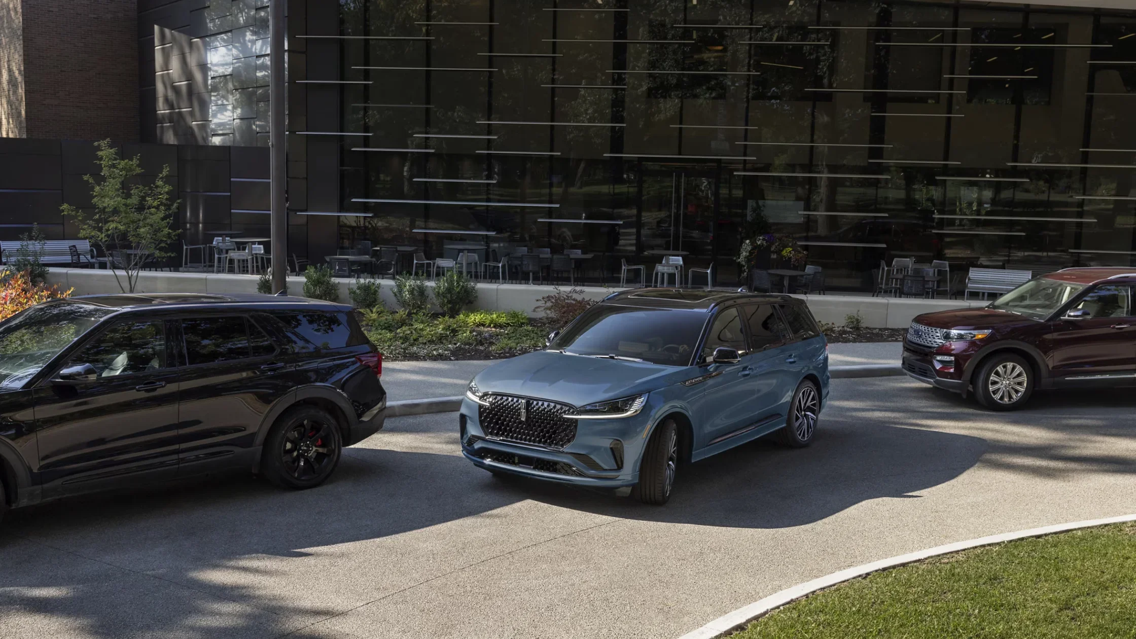 2025 Lincoln Black Label Aviator in blue parked between black and red SUVs in a modern urban setting.