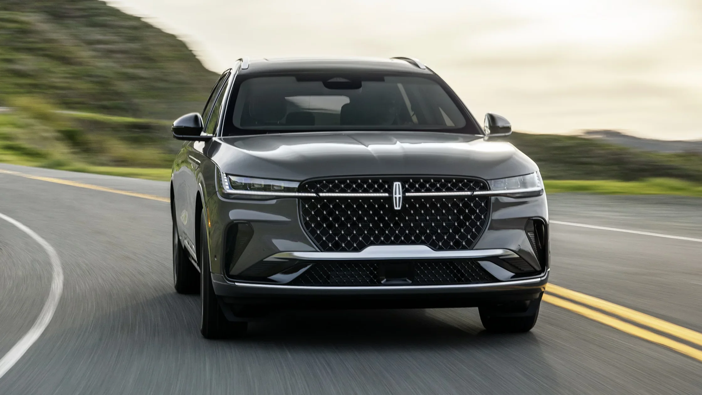 Lincoln Black Label Nautilus SUV driving on a winding road, highlighting its bold front grille, slim LED headlights, and aerodynamic design.
