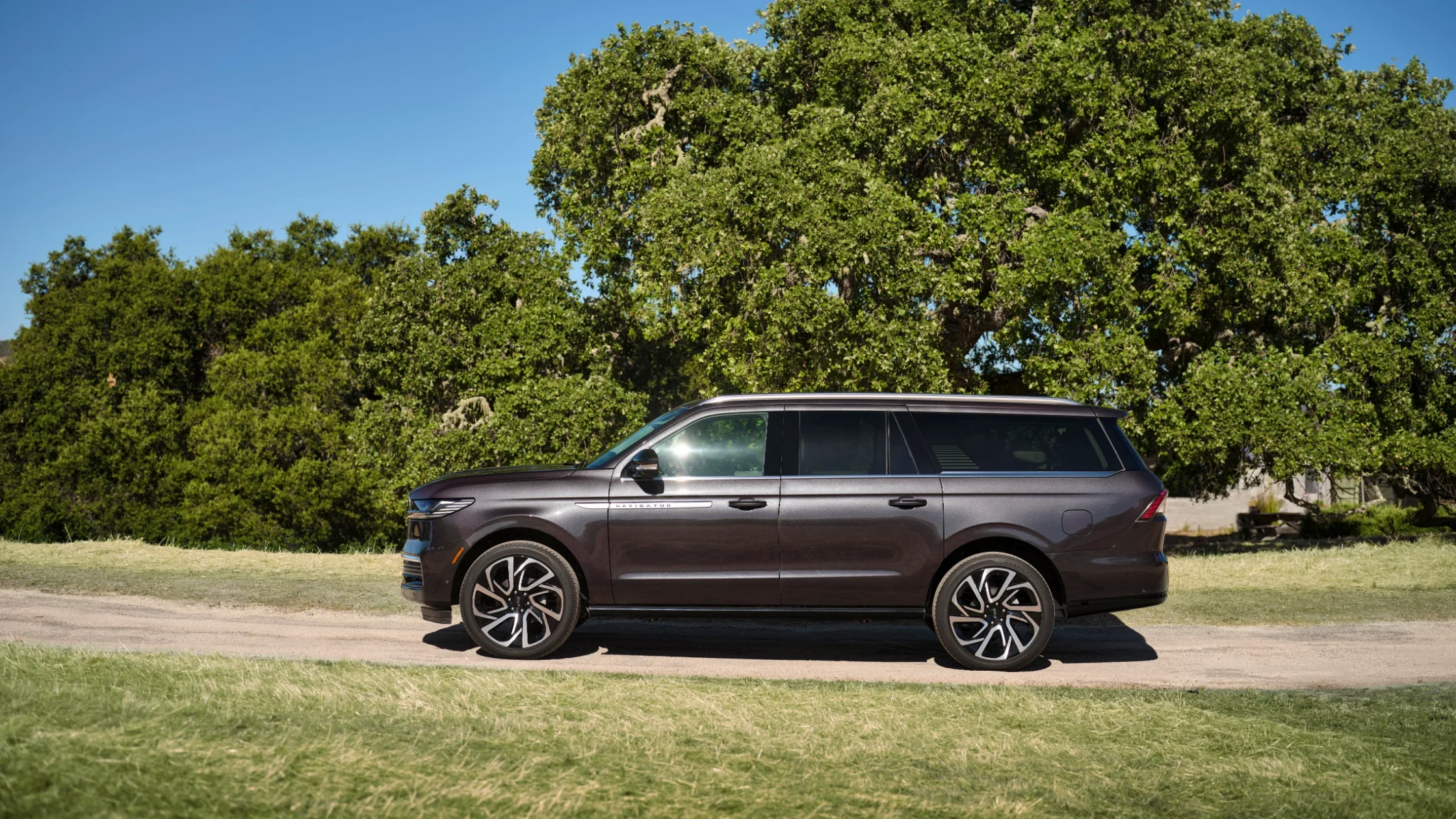 The 2025 Lincoln Navigator® Reserve parked on a scenic landscape, displaying its long, elegant profile with black alloy wheels, tinted windows, and a bold chrome grille.