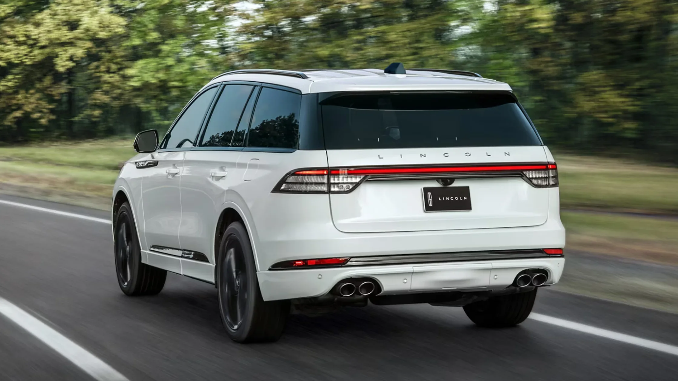 Rear angle of white 2025 Lincoln Aviator® SUV showing quad exhausts and full-width LED tail light