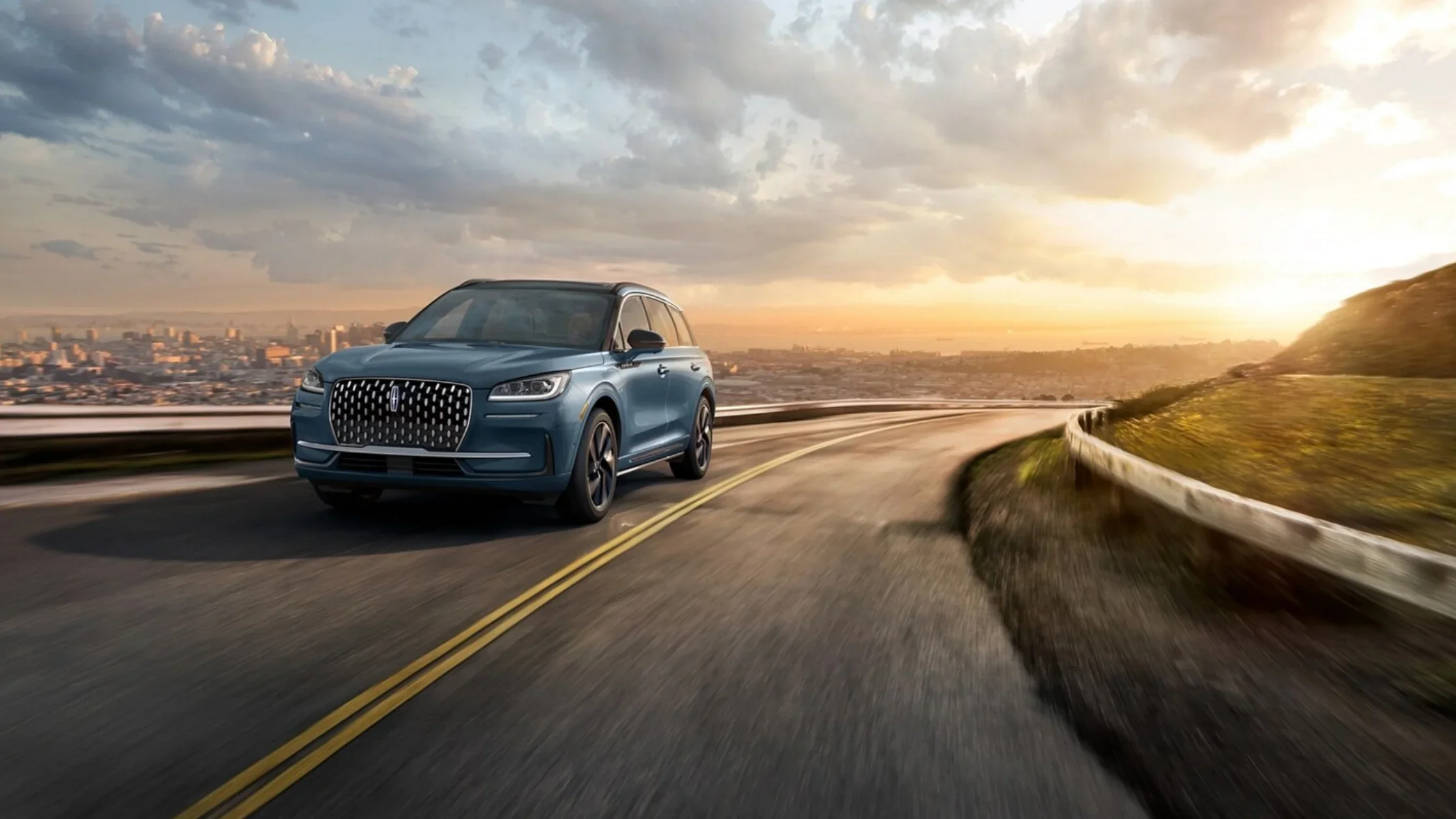 2025 Lincoln Corsair® in blue driving along a hillside highway with city skyline at sunset