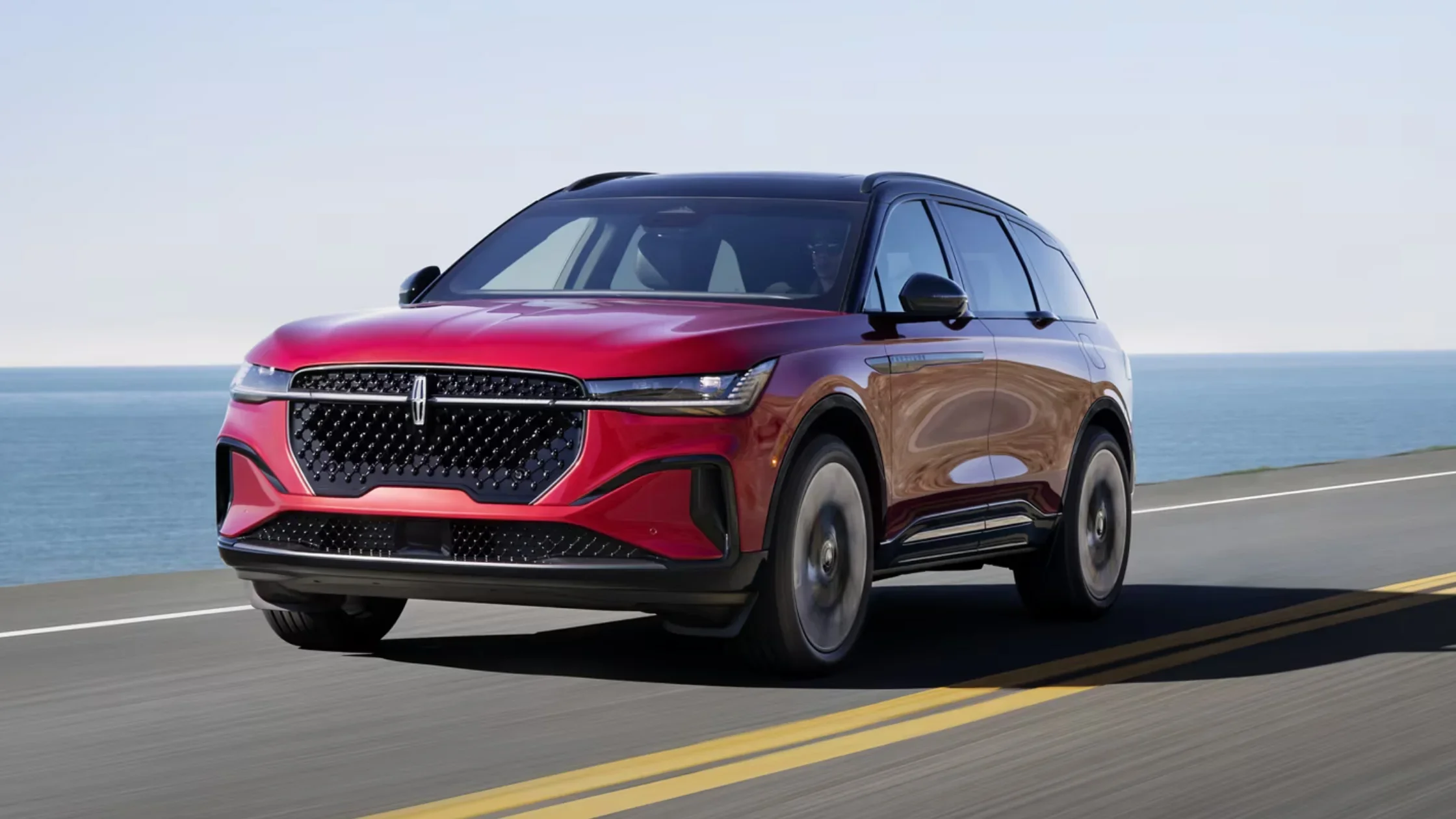 2025 Lincoln Nautilus® in red driving along coastal highway with ocean in the background.