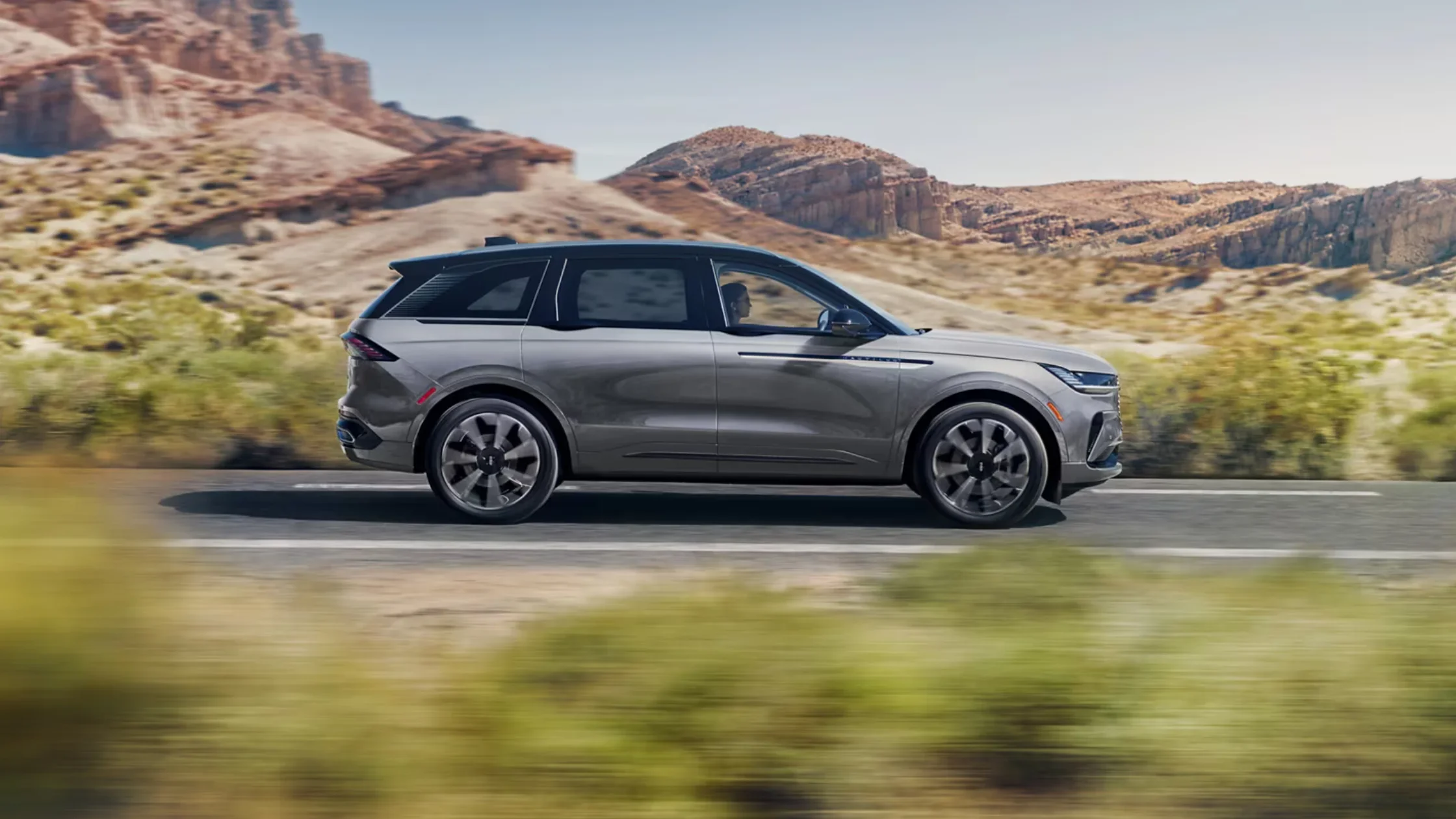 Side profile of silver 2025 Lincoln Nautilus® in motion through desert road with rocky landscape