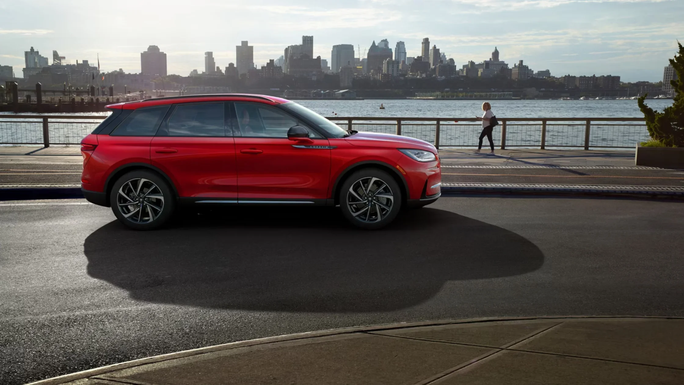 2025 Corsair Reserve luxury SUV exterior in bold red near waterfront city skyline.